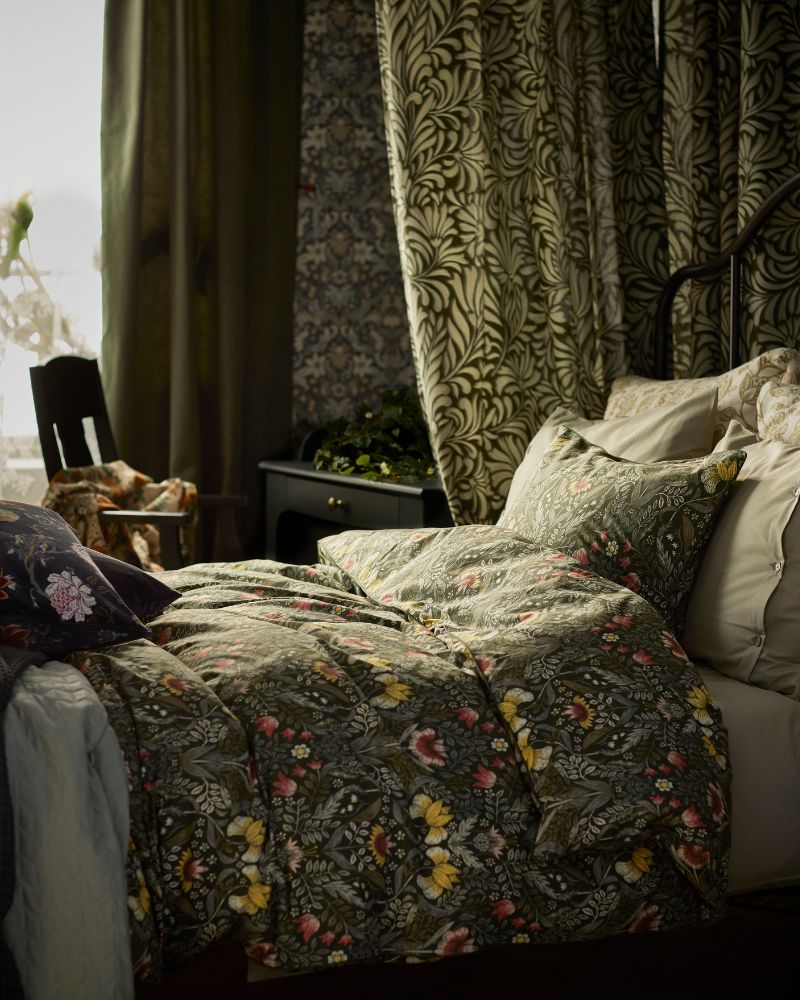Dark green/multicolour KÄRRDUNÖRT bed linen on a bed that’s surrounded by patterned curtains, near a window.
