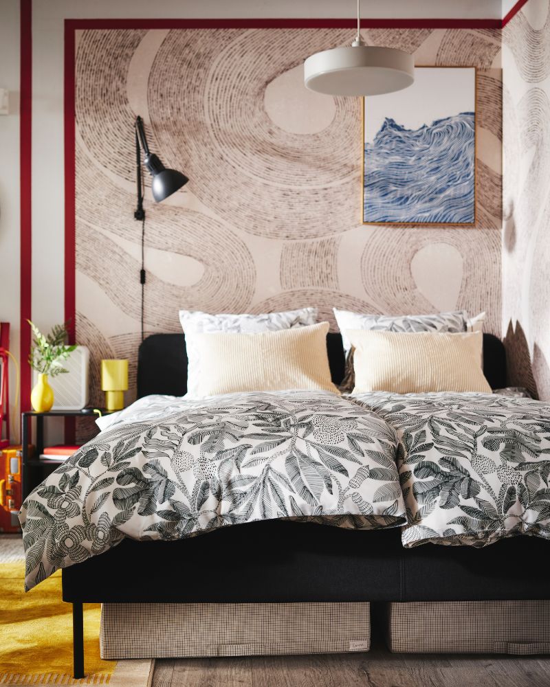 A dark grey SLATTUM upholstered bed in the corner of a bedroom with two duvets covered in BROKDRACENA bed linen.