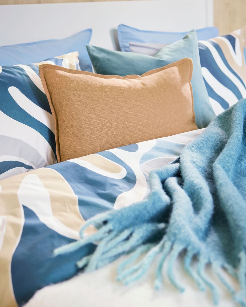 A close-up of a bed with a leafy-patterned MYGGLASVINGE quilt cover and pillowcases accented by a grey-turquoise throw.