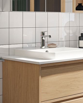 White sink with chrome faucet on a wooden vanity against tiled wall.