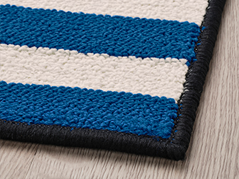 Close-up of a blue and white striped rug, with black trim and woven texture. Add color and comfort to your space.