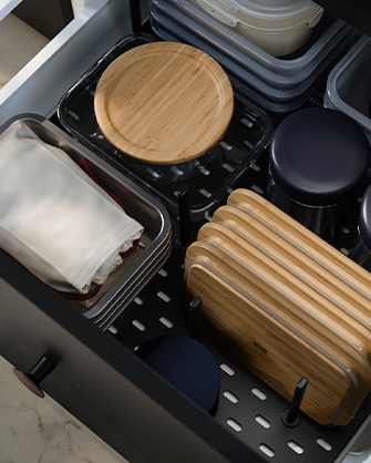 Cajón oscuro con un sistema de organización modular, almacenando tablas de cortar y utensilios, con separadores para optimizar el espacio.