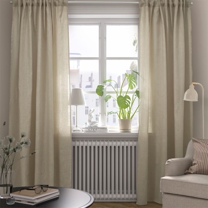 Window with long light beige curtains and a Monstera plant on the windowsill. A radiator below the window and a seating area with an armchair and low table.