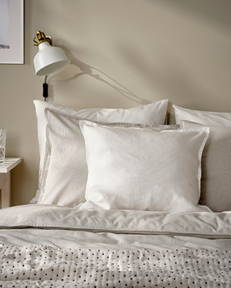 Bed with light-colored bedding and a polka-dot duvet. A white wall lamp illuminates the headboard, adding warmth to the bedroom.