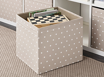 Cajón de almacenaje beige con lunares blancos de IKEA, con un juego de ajedrez y libros. Solución decorativa para estanterías, ideal para salones.