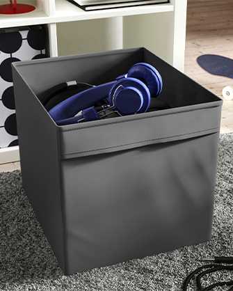 Cajón de almacenaje gris oscuro de IKEA con auriculares azules. Solución funcional para organizar dispositivos electrónicos y cables en salones o salas de juegos.
