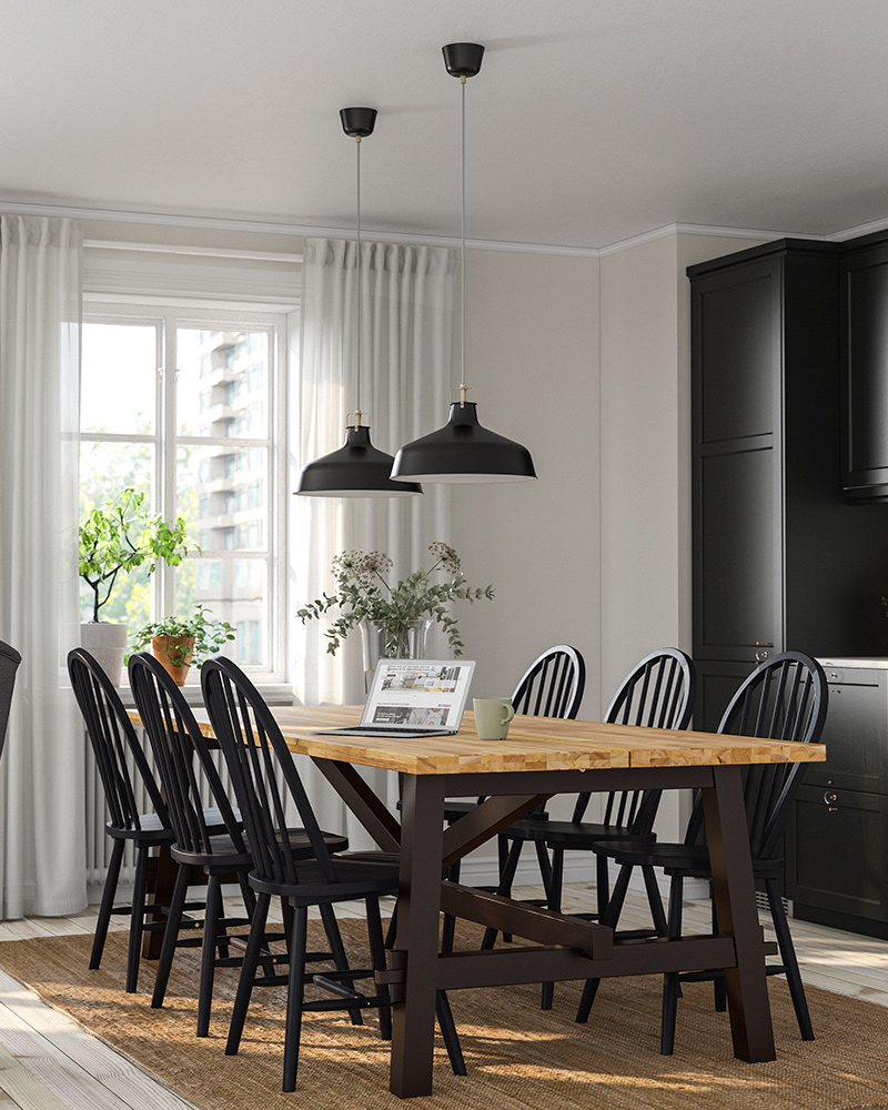 A SKOGSTA table and several black SKOGSTA chairs, two RANARP pendant lamps lighting the dining room