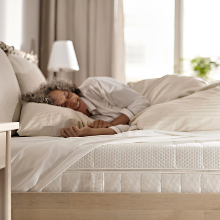 A woman smiling peacefully in a bed with white sheets and duvet.