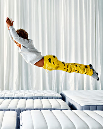 A child jumping in the air over multiple mattresses.