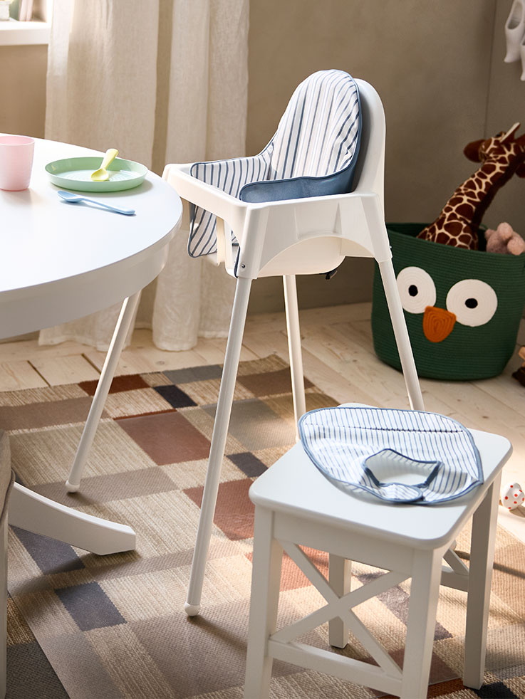 Un taburete ROSENTORP blanco y una trona ANTILOP con bandeja están junto a una mesa extensible ROSENTORP blanca.