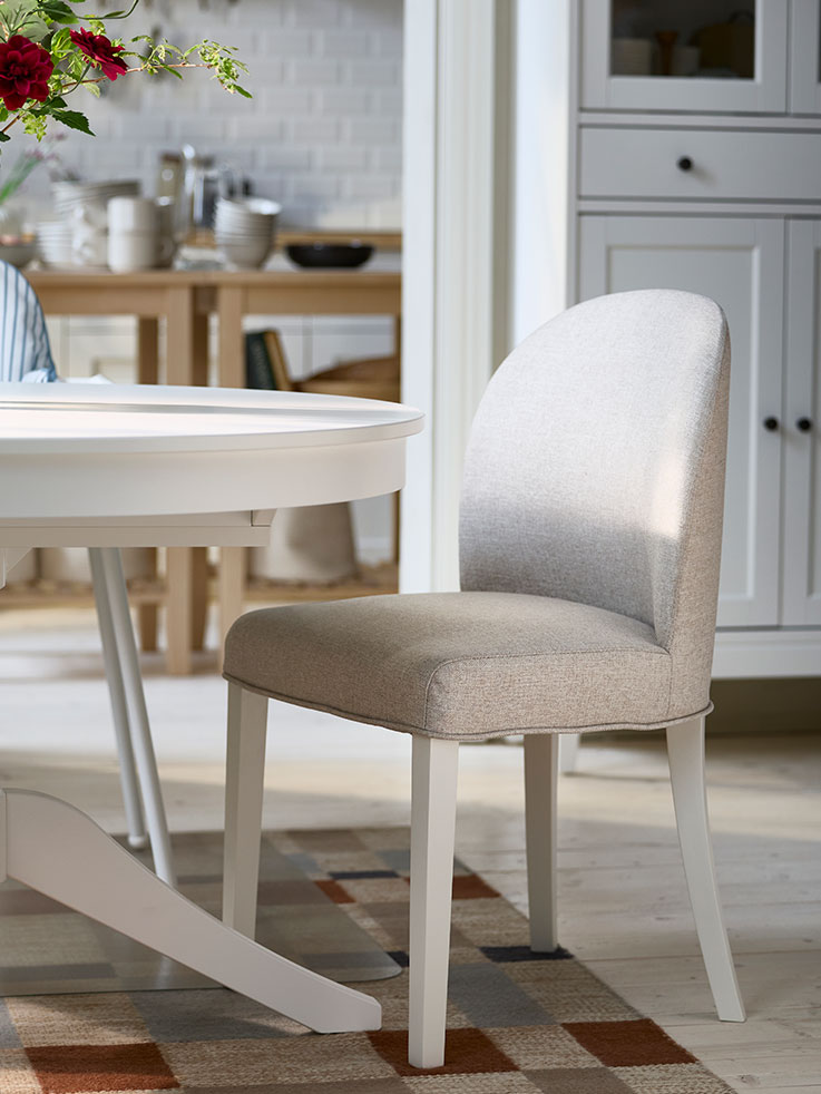 Una silla ROSENTORP totalmente tapizada en Kilanda beige claro/blanco se coloca junto a una mesa extensible ROSENTORP blanca.