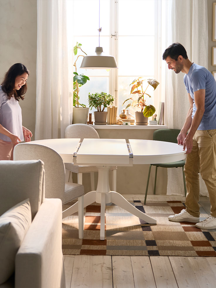 Dos personas están sacando una mesa extensible ROSENTORP blanca y redonda para hacerla más grande con el extenso