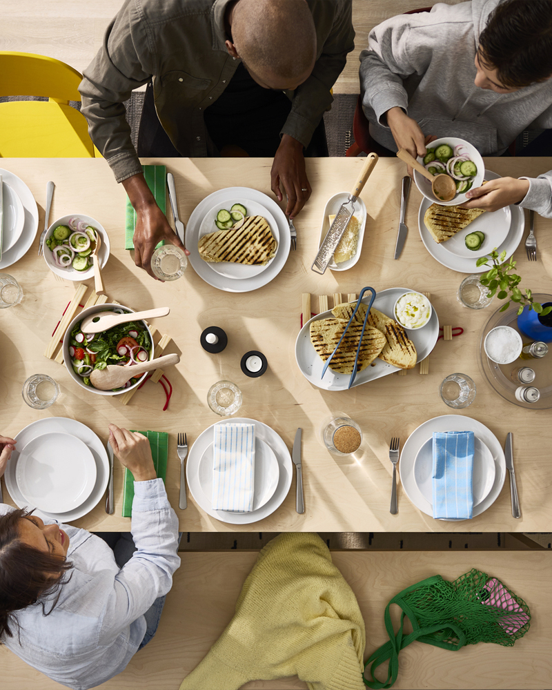 A bird’s-eye view of a BERGSHYTTAN table in birch veneer where people are sharing a meal together on white GODMIDDAG plates.