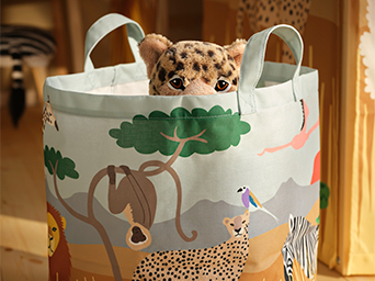Round fabric storage basket with handles and a safari print, with the head of a stuffed leopard peeking over the rim.