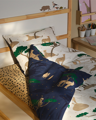 Children's bed with light wood frame and cotton bedding featuring a leopard and tree print, in white, beige, and dark blue colors.
