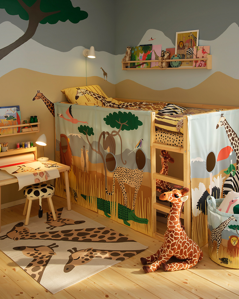 Habitación infantil decorada con juguetes temáticos de sabana de la colección SANDLÖPARE, con jirafas tanto en la alfombra como en la ropa de cama.
