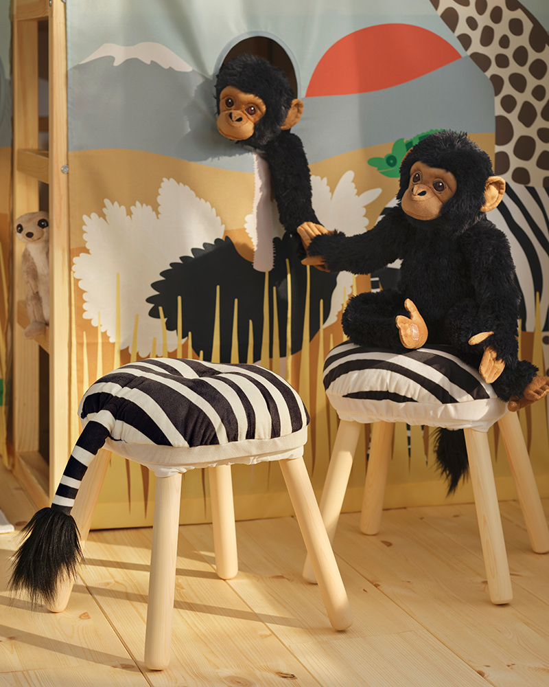 Dos chimpancés de peluche negros de la colección SANDLÖPARE se toman de la mano en una luminosa habitación infantil con temática de sabana.