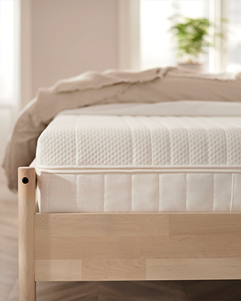 Colchón blanco sobre estructura de cama de madera natural en dormitorio luminoso. Ropa de cama limpia y luz natural suave crean un espacio de descanso tranquilo