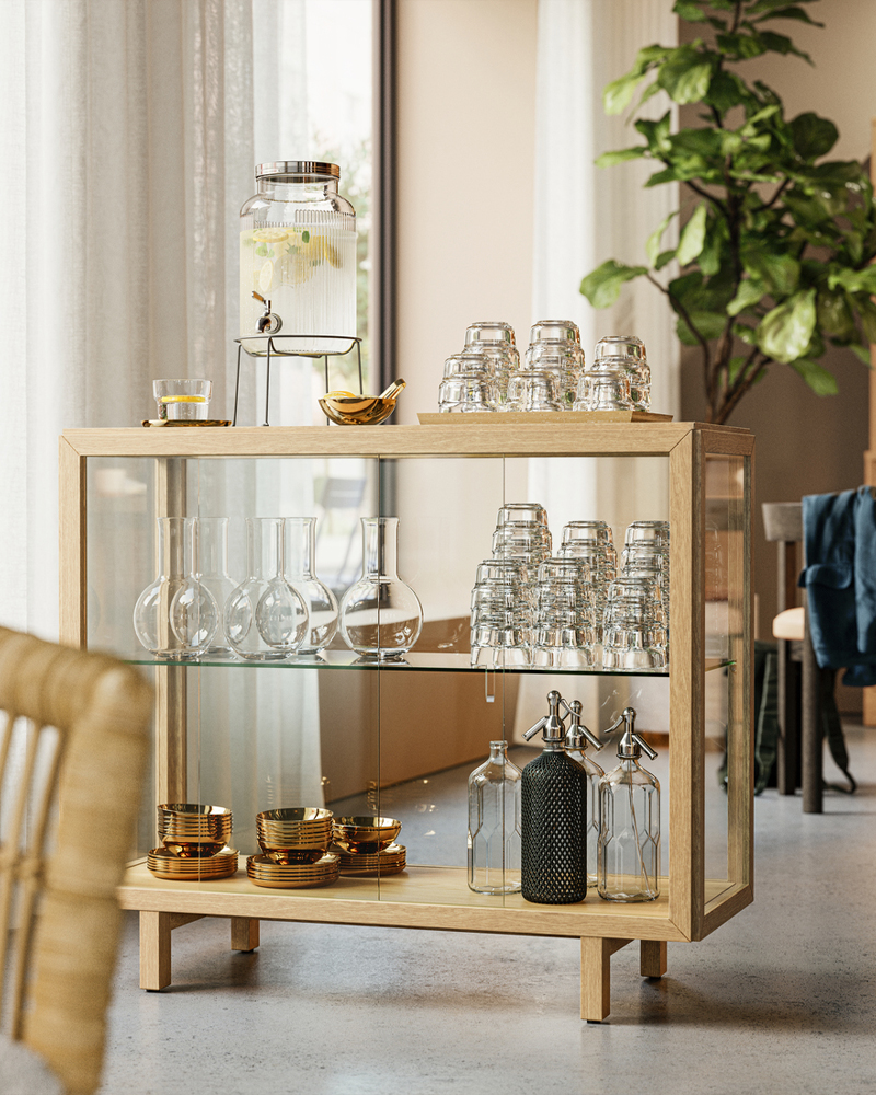 Un armario con puertas de cristal STOCKHOLM 2025 con chapa de roble natural en el vestíbulo de un hotel que crea una zona de bebidas con refrescos.