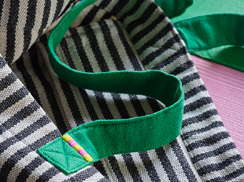 Bolso tote MÄVINN de rayas blancas y negras en algodón/hilo con asas verdes y un detalle bordado.