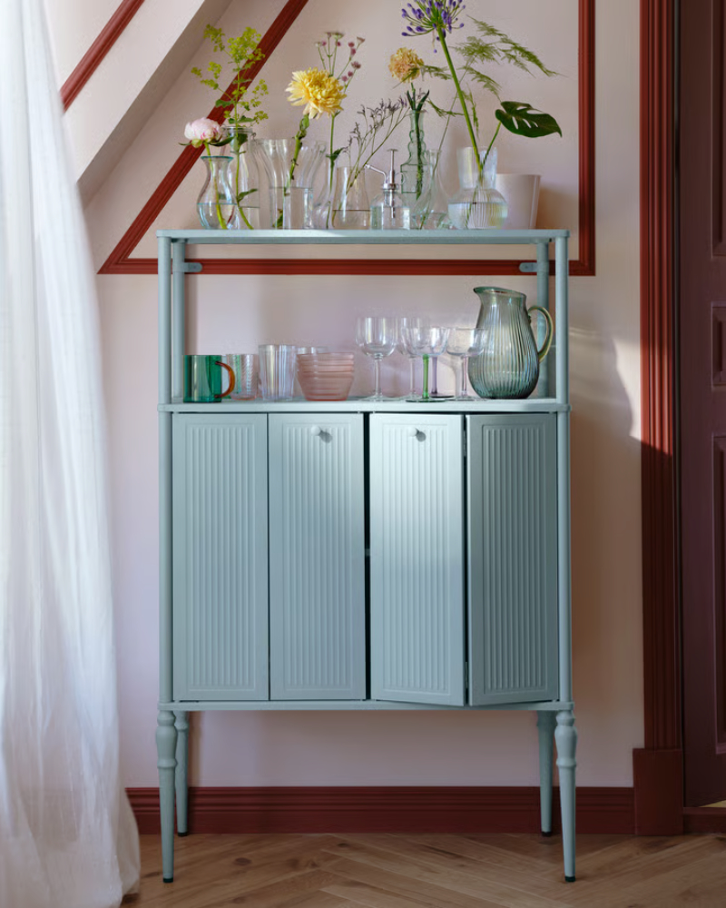 Un armario SÅGMÄSTARE gris azulado claro con tarros de cristal y vasos encima, colocado con elegancia en un interior con estilo.