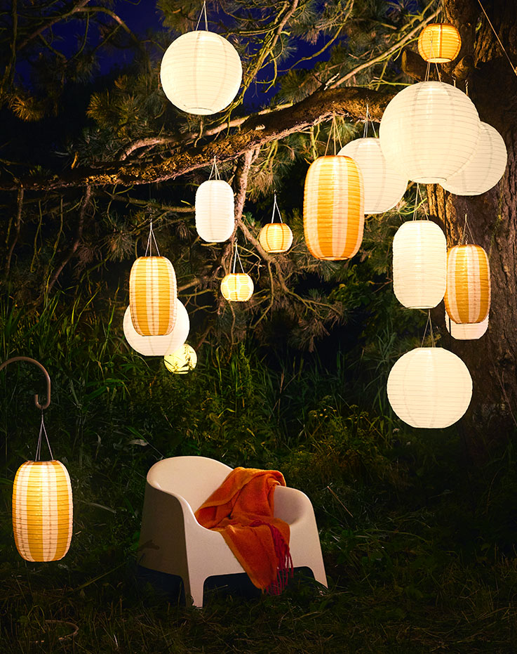 Un jardín nocturno con una silla blanca y muchas lámparas colgantes SOLVINDEN blancas y naranjas alimentadas con energía solar