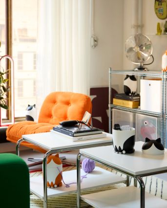 Three cat-shaped GRESIMOJS storage with lid are on tables and shelves in a room. Two are black/white. One is orange/white.