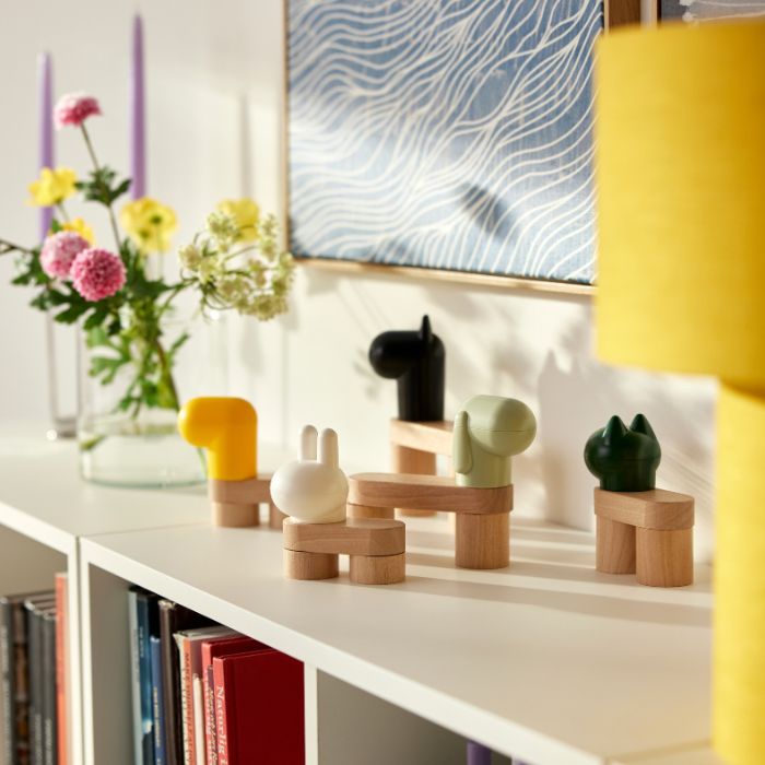 In a bright room, sunlight casts shadows on the wall from a set of GREJSIMOJS toy building blocks decorating a bookcase.