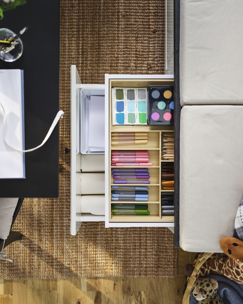 Cajones con bandeja para cubiertos UPPDATERA, llenos de bolígrafos de colores, pinceles y pinturas junto a una mesa negra.
