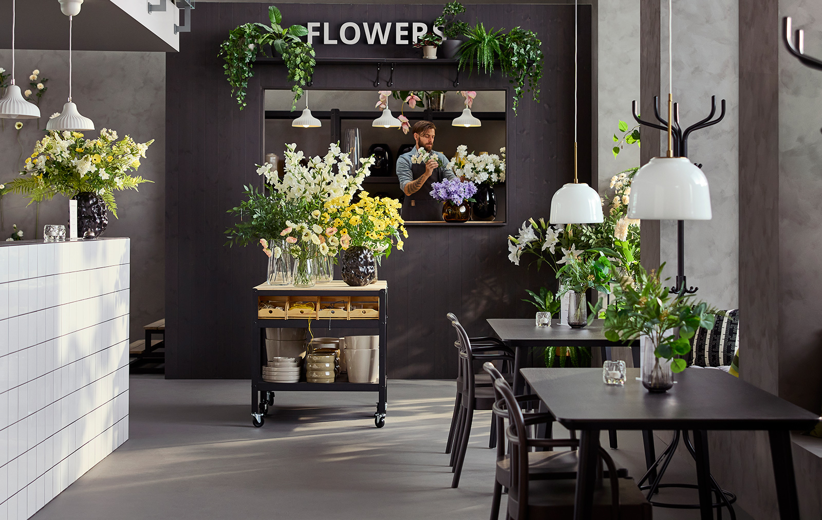 Café environment with natural light featuring tables, chairs and a black/pine BROR trolley displaying flowers and vases.