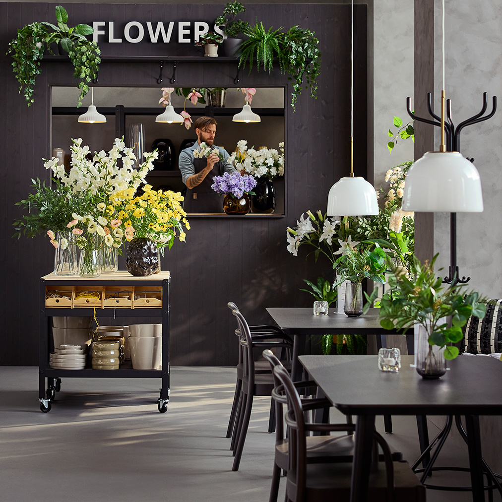 Café environment with natural light featuring tables, chairs and a black/pine BROR trolley displaying flowers and vases.