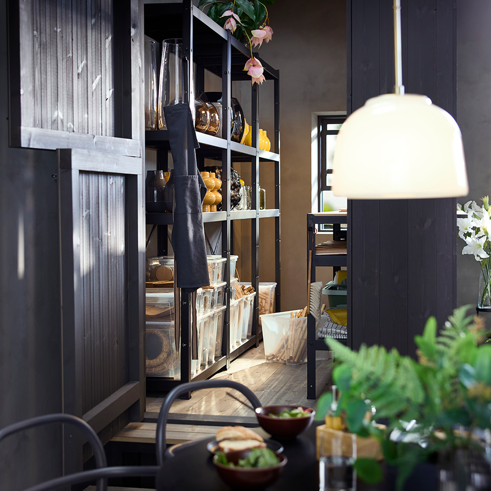 A shop storage with black BROR shelving unit displaying transparent boxes, vases and plants on its shelves.