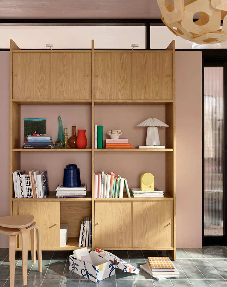 Un luminoso salón con una combinación de muebles de almacenamiento LÅDMAKARE en roble claro con puertas correderas, con libros y objetos decorativos.
