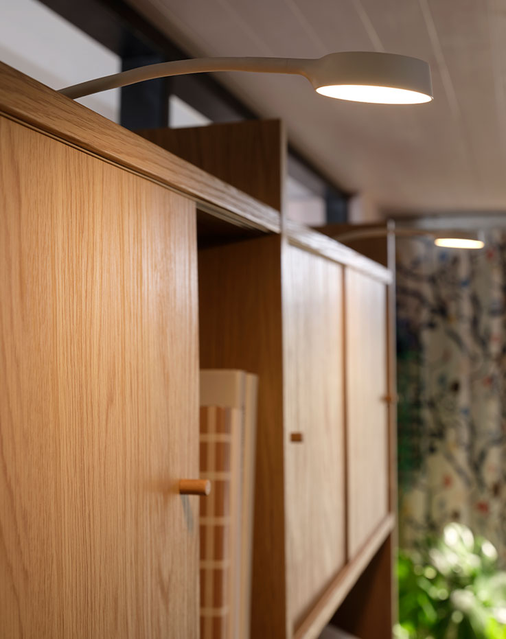 Iluminación de armario Lit YTBERG montada en la parte superior de un mueble combinado LÅDMAKARE con puertas correderas en una luminosa sala de estar.