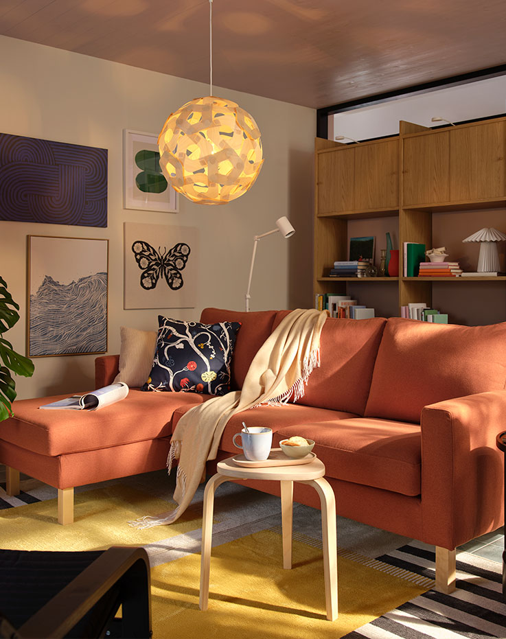 Una sala de estar con un sofá de tres plazas SALTSJÖBADEN de color marrón rojizo con chaise longue, rodeado de una decoración moderna y plantas.