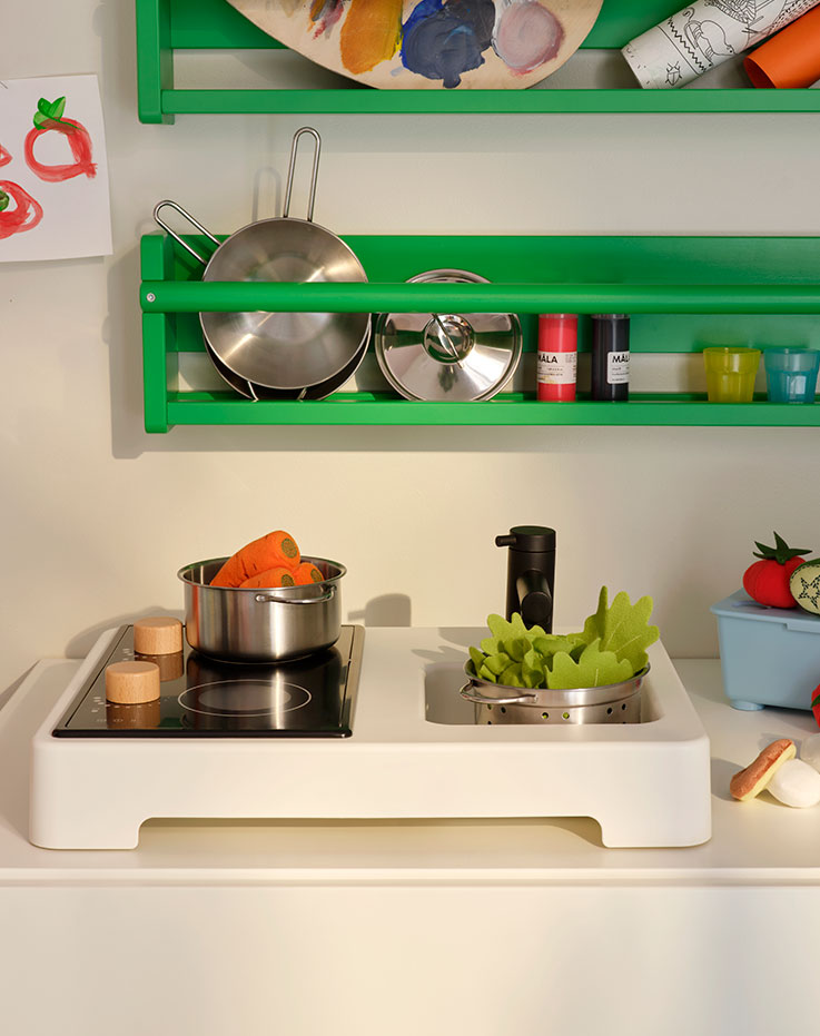 Partes de una mini cocina de juguete STENMUS debajo de un armario de pared verde FLISAT, todo ello lleno de accesorios de cocina de juguete.