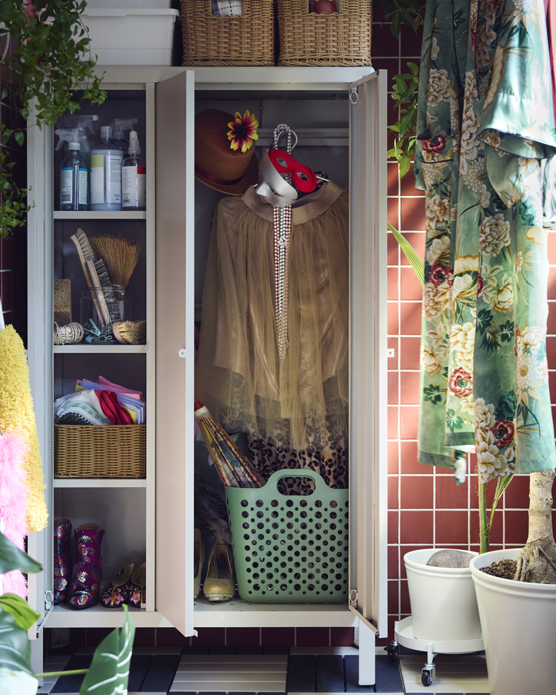 Un balcón con un armario KOLBJÖRN beige para almacenamiento, con cestas y productos de limpieza. Hay plantas de interior cerca.
