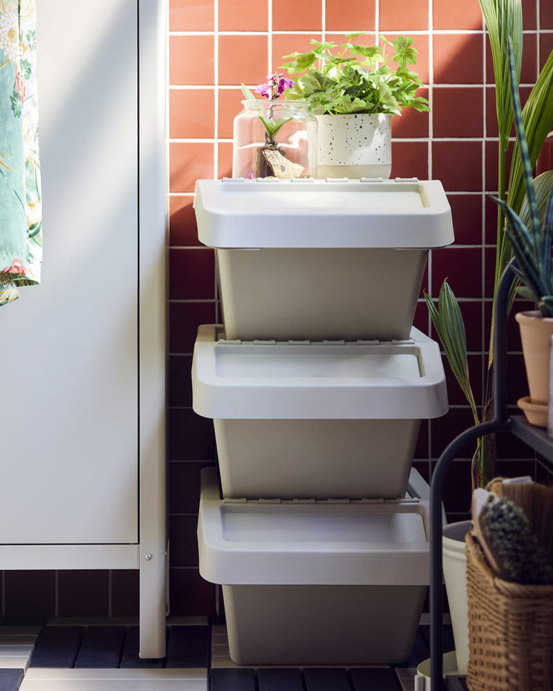 Un balcón con tres cubos de basura SORTERA de color beige con tapa apilados uno encima del otro contra una pared de azulejos rosas.