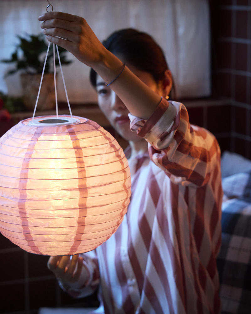 Primer plano de una mano sosteniendo una lámpara colgante SOLVINDEN LED de energía solar de color rosa, con un diseño redondo en forma de globo.