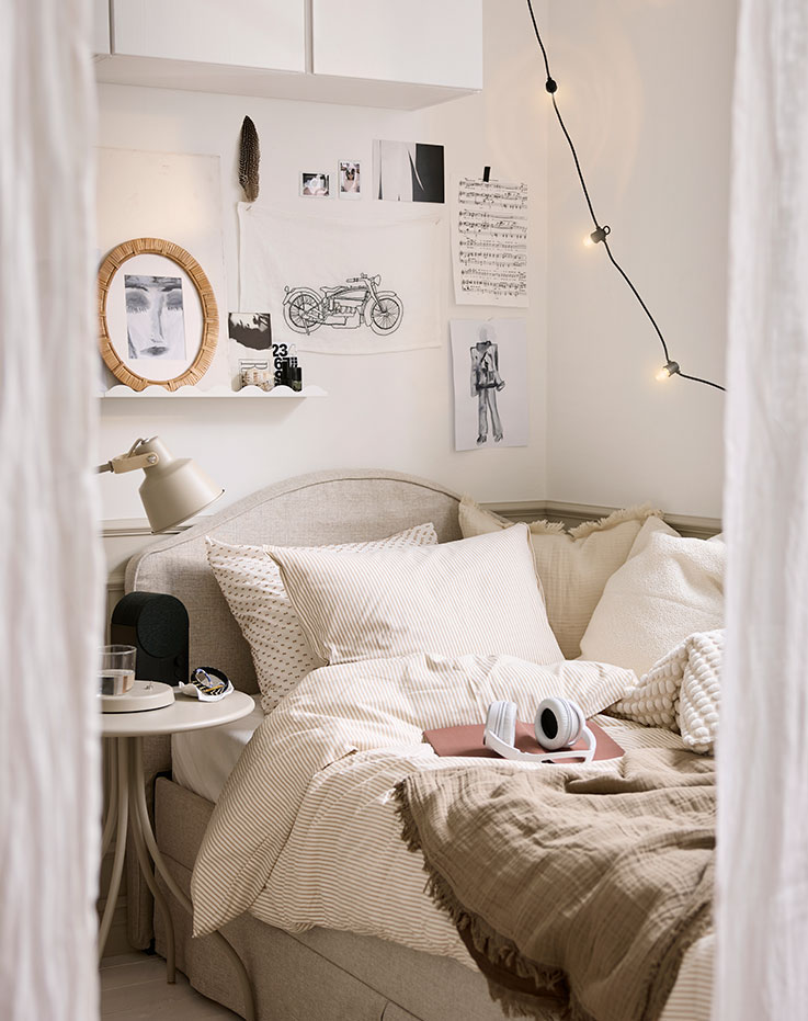 Una escena en el dormitorio con un edredón SOLFIBBLA en color blanco roto y una funda de almohada cuidadosamente colocados sobre una cama con ropa de cama a rayas en tonos neutros.