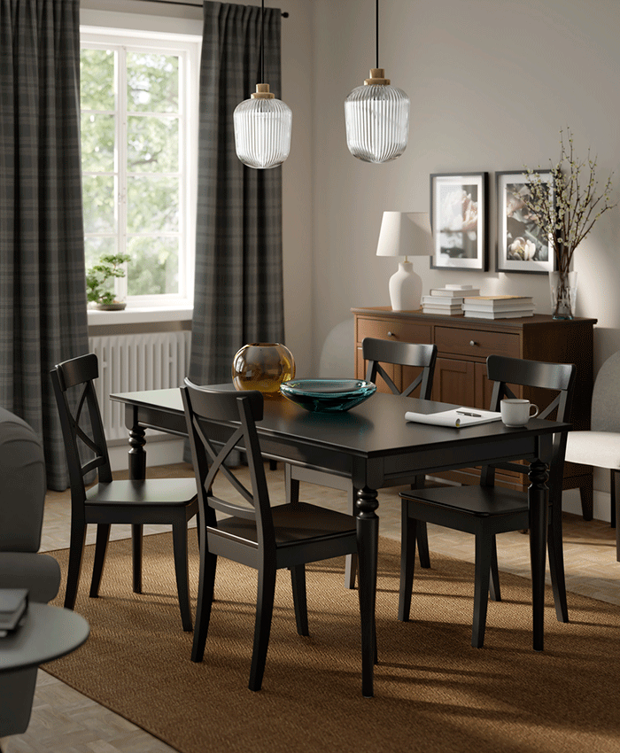 Mesa de comedor negra con sillas de respaldo en aspa sobre alfombra marrón. Un aparador de madera oscura y lámparas de vidrio estriado crean un ambiente acogedor.