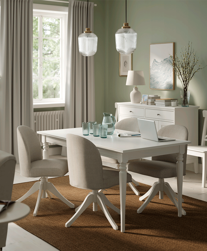 Mesa de comedor blanca con sillas giratorias tapizadas en beige. Paredes verdes, aparador blanco y cortinas claras aportan un estilo luminoso y moderno.