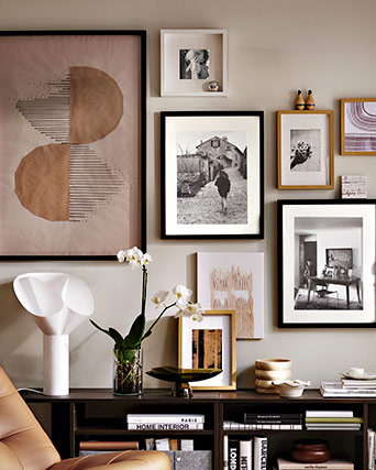 Gallery wall with abstract art and black and white photos above a sideboard with books, a white orchid, and decorative objects.