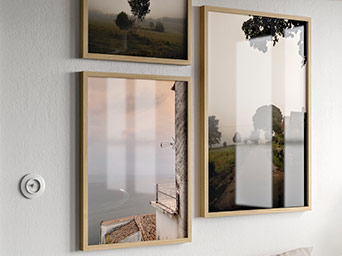 Three framed prints featuring misty landscapes and trees in light wood frames, arranged symmetrically on a textured white interior wall.