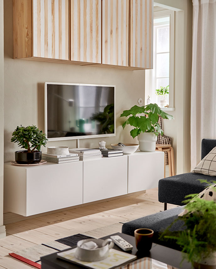 Un mueble para TV BESTÅ blanco con puertas está montado en la pared debajo de un televisor montado en la pared y armarios IVAR pintados con rayas.