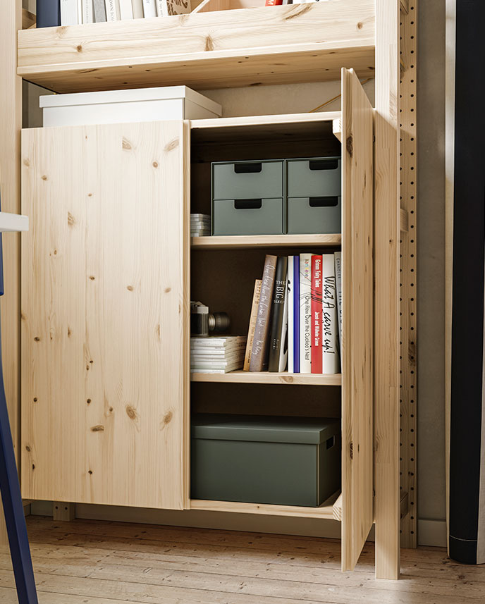 Un espacio luminoso con una estantería IVAR, una puerta de armario de pino abierta que deja ver libros y cajas de almacenamiento ordenados cuidadosamente.