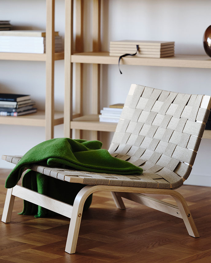 Una sala de estar con un sillón STOCKHOLM 2025 verde de chapa de abedul con asiento tejido, acompañado de una manta doblada.