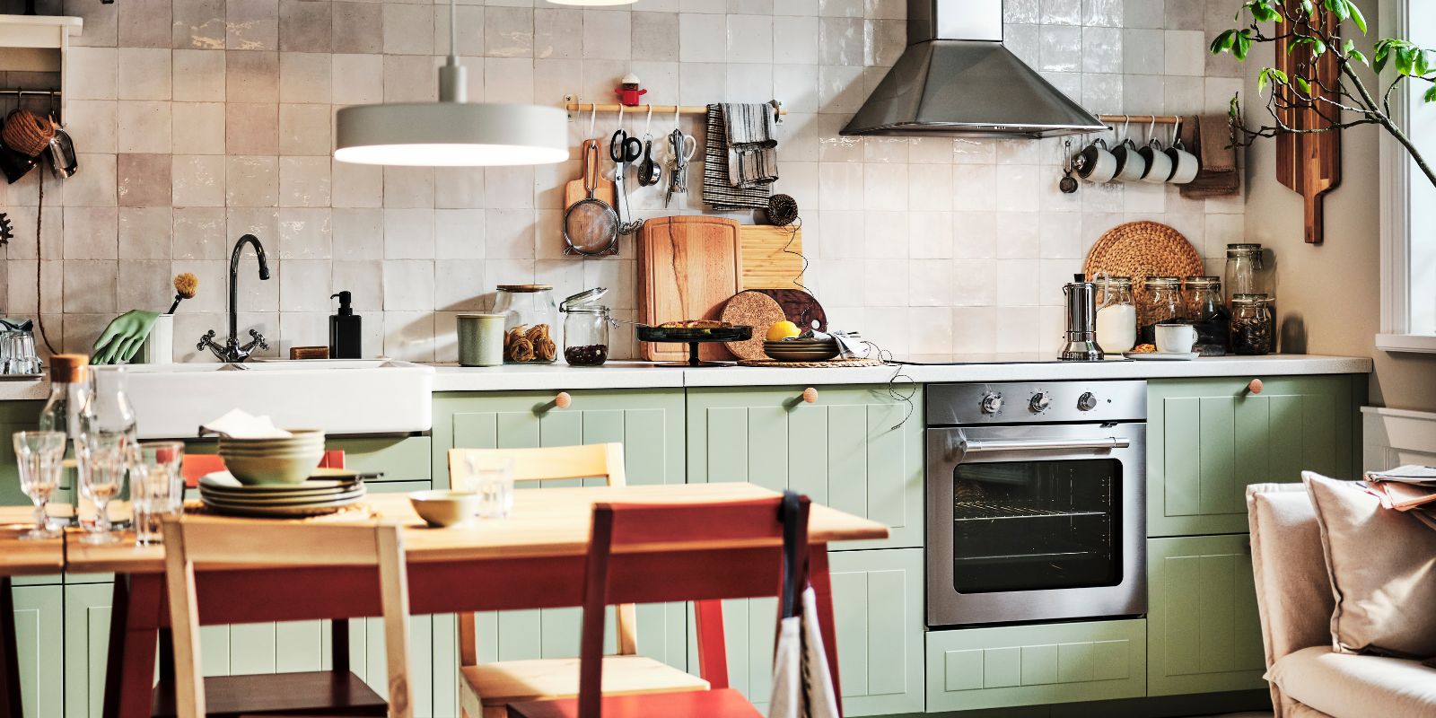 Cocina con puertas STENSUND verdes, pared de azulejos, campana de acero y utensilios colgantes en un ambiente rústico y cálido.