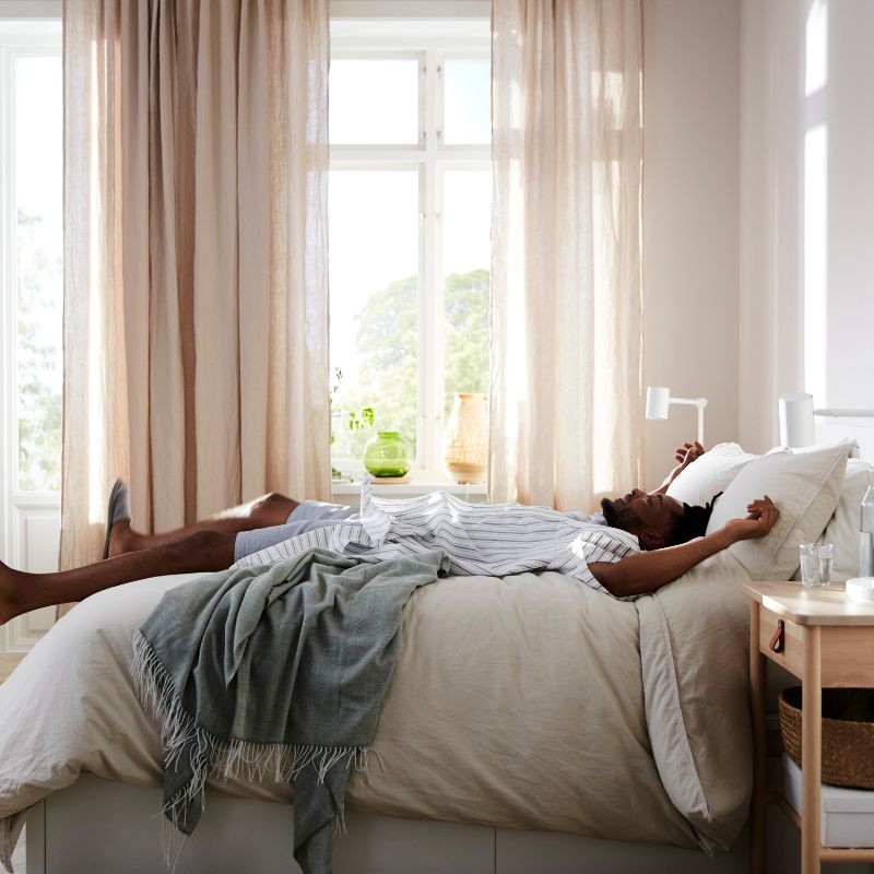 Dormitorio luminoso con cama MALM, lámpara NYMÅNE y cortinas HÄLLEBRÄCKA creando un ambiente cálido y relajante.