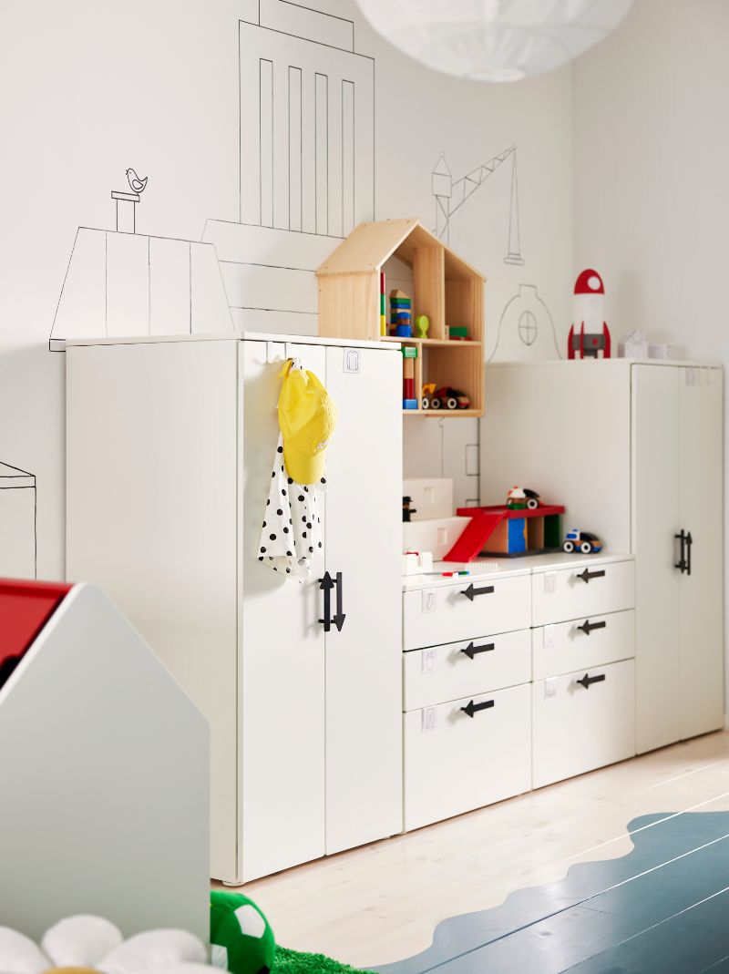 Muebles de almacenamiento SMÅSTAD/PLATSA blancos con tiradores JÄRNSPARV negros contra una pared con una casa de muñecas/estantería FLISAT encima.